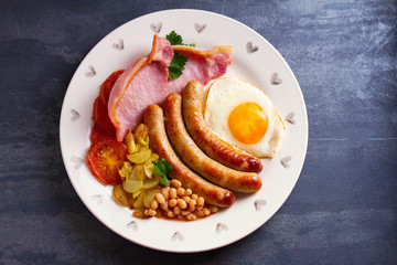 Sausages, bacon, egg, tomatoes, fries and beans on white plate. Overhead horizontal image