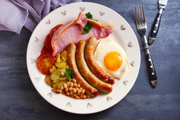 Sausages, bacon, egg, tomatoes, fries and beans on white plate. Overhead horizontal image