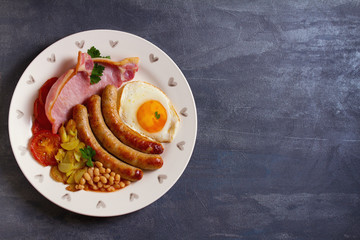 Sausages, bacon, egg, tomatoes, fries and beans on white plate. Overhead horizontal image, copy space, room for text