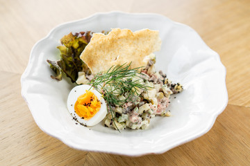 Russian traditional salad Olivier with vegetables and meat. Salad on a plate on a wooden plate. Menu restaurant. Russian traditional salad