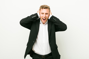 Young caucasian business man covering ears with hands trying not to hear too loud sound.