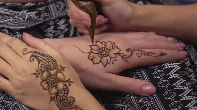Master is performing mehndi beauty treatments. Woman is decorating hands of client girl by temporary henna tattoos