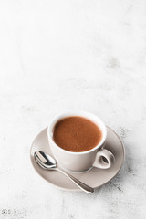 Cup of hot cocoa or hot chocolate or americano in white cup isolated on bright marble background. Overhead view, copy space. Vertical photo. traditional drinks for winter time