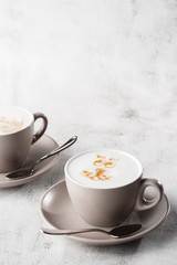 Two white cups of hot latte coffee with beautiful milk foam latte art texture isolated on bright marble background. Overhead view, copy space. Advertising for cafe menu. Vertical photo.