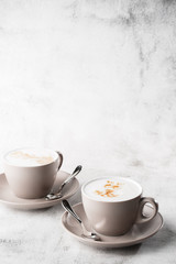 Two white cups of hot latte coffee with beautiful milk foam latte art texture isolated on bright marble background. Overhead view, copy space. Advertising for cafe menu. Vertical photo.