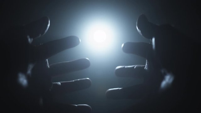 A mans hand reaches towards the light and fingers play with the light and pass over the source. Religion, spirituality and magic concepts.