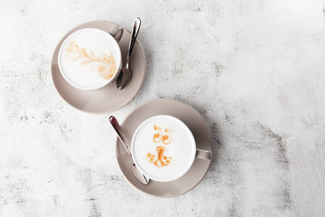 Two white cups of hot latte coffee with beautiful milk foam latte art texture isolated on bright marble background. Overhead view, copy space. Advertising for cafe menu. Horizontal photo.