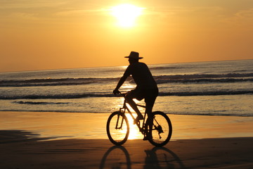 Fototapeta na wymiar Man silhouette bycicling on the beach during the sunset. Golden sky with the sun in the sky. Riviera beach, Bertioga, Brazil