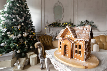 Gingerbread house, concept holiday of Christmas and Happy new year. Defocused lights of Christmas tree. Morning in the bright living room. Holiday mood.