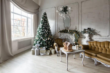 Christmas morning. Classic luxury apartments with a white fireplace, christmas tree, sofa, large windows and chandelier.