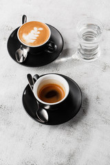 Two dark cups of hot black coffee, espresso, cappuccino with milk isolated on bright marble background. Overhead view, copy space. Advertising for cafe menu. Coffee shop menu. Vertical photo.
