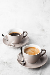 Two white cups of hot black coffee with milk isolated on bright marble background. Overhead view, copy space. Advertising for cafe menu. Coffee shop menu. Vertical photo.