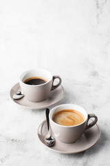 Two white cups of hot black coffee with milk isolated on bright marble background. Overhead view, copy space. Advertising for cafe menu. Coffee shop menu. Vertical photo.
