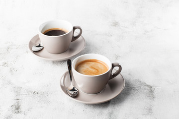 Two white cups of hot black coffee with milk isolated on bright marble background. Overhead view,...