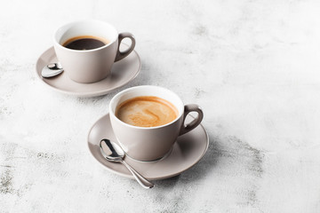 Two white cups of hot black coffee with milk isolated on bright marble background. Overhead view, copy space. Advertising for cafe menu. Coffee shop menu. Horizontal photo.