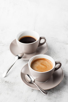 Two white cups of hot black coffee with milk isolated on bright marble background. Overhead view, copy space. Advertising for cafe menu. Coffee shop menu. Vertical photo.