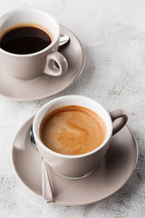 Two white cups of hot black coffee with milk isolated on bright marble background. Overhead view, copy space. Advertising for cafe menu. Coffee shop menu. Vertical photo.