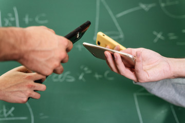 Students using mobile phones in classroom with a chalkboard in the background .