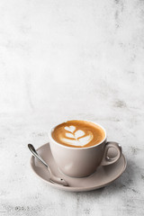 White cup of hot latte coffee with beautiful milk foam latte art texture isolated on bright marble background. Overhead view, copy space. Advertising for cafe menu. Coffee shop menu. Vertical photo.