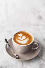White cup of hot latte coffee with beautiful milk foam latte art texture isolated on bright marble background. Overhead view, copy space. Advertising for cafe menu. Coffee shop menu. Vertical photo.