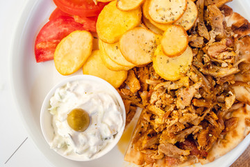 Close up view high angle on gyros in plate with pork meat pig and potato chips and tzatziki salad and tomato