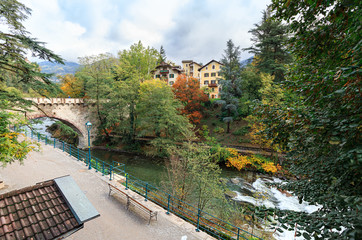 Fototapeta premium Embankment of the Passer river in the fall. View of the Steinerner Steg bridge - oldest bridge in the town. Town of Merano, Trentino-Alto Adige region, South Tyrol, Italy.