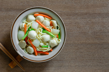 top view of stir fried japanese noodles with fish ball and vegetables in a ceramic dish on wooden table. asian homemade style food concept.