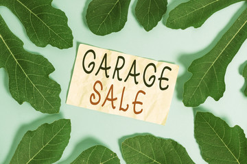 Conceptual hand writing showing Garage Sale. Concept meaning sale of miscellaneous household goods often held in the garage Leaves surrounding notepaper above empty soft pastel table