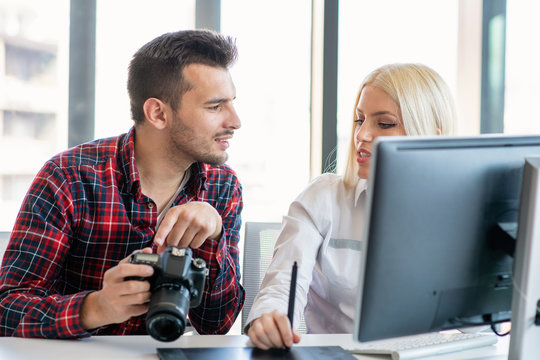 Graphic designer wearing casual clothes talking with colleague while using graphics tablet at the studio