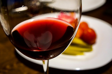 red wine in a glass opposite a plate with a delicious dinner, still life on a dark background, noble alcohol close up