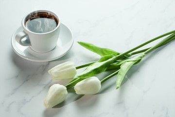 coffee background of a cup of hot black coffee with bunch of white tulip on white marble background