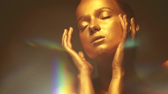 Fashion model woman in golden bright sparkles posing in studio, portrait of beautiful sexy girl with golden skin. Glitter gold metallic shine makeup. Slow motion 4K UHD video footage. 3840X2160