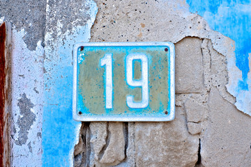 Number 19, nineteen, weathered plate on an old colorful decayed blue wall.