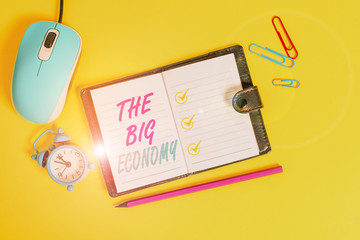 Word writing text The Big Economy. Business photo showcasing Global finances Worldwide Market Trade Money exchange Locked diary sheets clips marker mouse alarm clock colored background