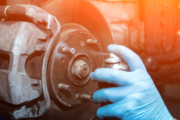 Close-up Workshop worker in protective gloves lubricates wheel studs, brake repair. Work at the...
