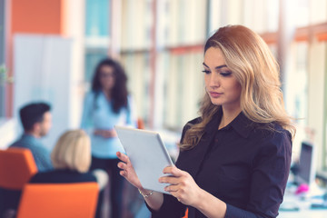 Portrait of happy businesswoman holding digital tablet in office standing in front of colleagues discussing at background