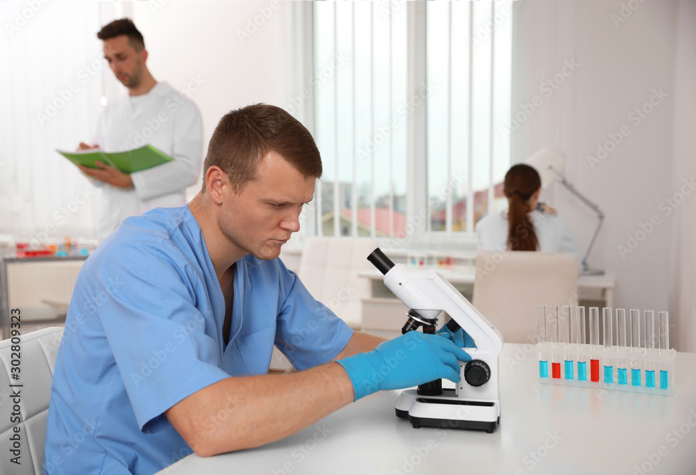 Poster Scientist with microscope at table and colleagues in laboratory. Medical research