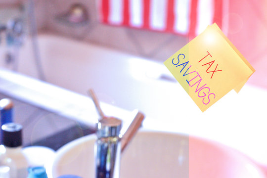 Word writing text Tax Savings. Business photo showcasing only a portion of income is taxable Pay a reduced amount of tax Piece of square yellow sheet use to give notation stick to washroom mirror