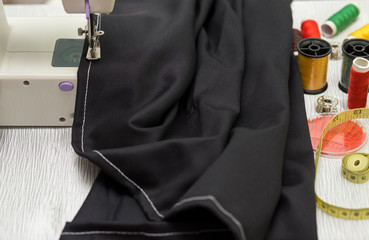 Sewing with black  fabric by using small sewing machine and accessories on table in workshop