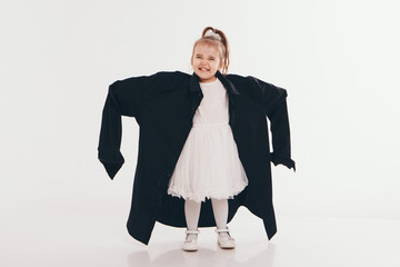 a little girl tries on dad's shirt. Child in big black clothes on white background. Concept of...