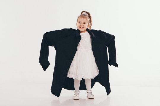 a little girl tries on dad's shirt. Child in big black clothes on white background. Concept of children's games, imitation of adult life, fashion