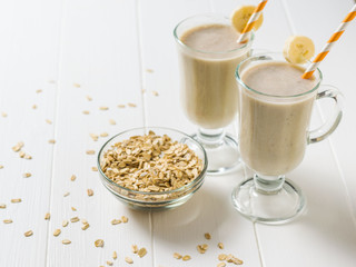 Banana smoothie and oatmeal scattered on a white wooden table. Vegetarian smoothie.