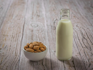 A bowl of almonds and a bottle of almond milk on a wooden table.