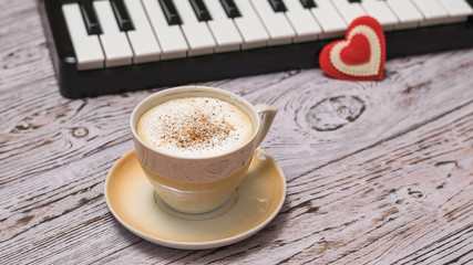 A red heart on the keys and a Cup of cinnamon coffee on the wooden table.