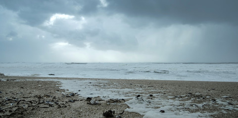 Cold windy beach in winter with stormy sky and hailstones on the sand