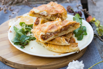 Lobiani - traditional baked Georgian pie with lobio beans and filo puff pastry. On plate with lemon slice, green rucola leaves and garlic. Homemade.