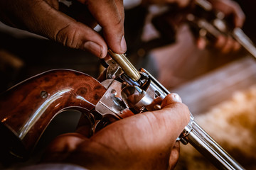 Closed up cowboy loading bullets into gun on hand before used to shot , vintage style.