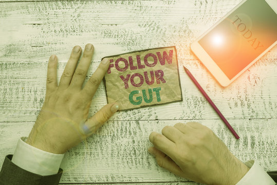 Text sign showing Follow Your Gut. Business photo text Listen to intuition feelings emotions conscious perception Hand hold note paper near writing equipment and modern smartphone device
