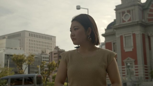 Close up of worried Asian woman thinking deeply with anxious facial expression ideal for female awareness campaign with cityscape, busy road, passing cars and skyline as background during daytime