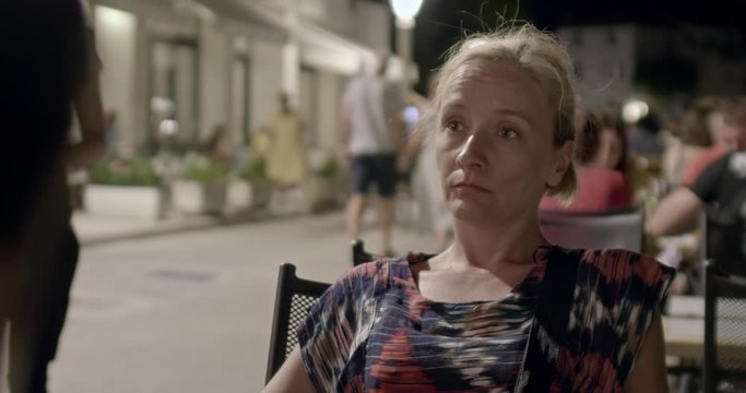 A woman with a bored expression takes part in a conversation at an outdoors restaurant